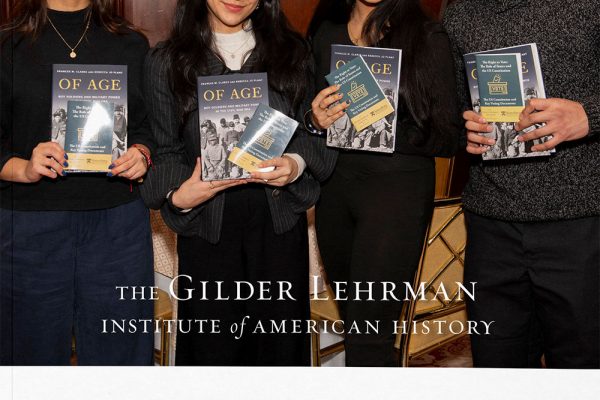 Four young adults stand indoors, smiling and holding books, in front of a backdrop that reads “The Gilder Lehrman Institute of American History 2025 Annual Report.” Their presence highlights the students’ role in the redesigned annual report, emphasizing storytelling that brings history to life.